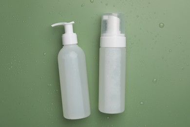 Photo of Wet bottles of face cleansing product on green background, flat lay