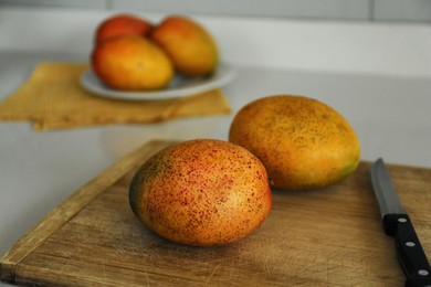 Photo of Tasty mangoes and knife on wooden board indoors
