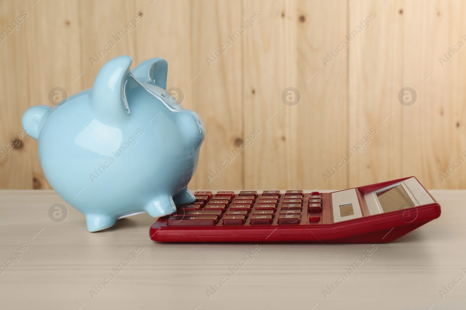 Photo of Calculator and piggy bank on light wooden table