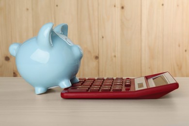 Calculator and piggy bank on light wooden table