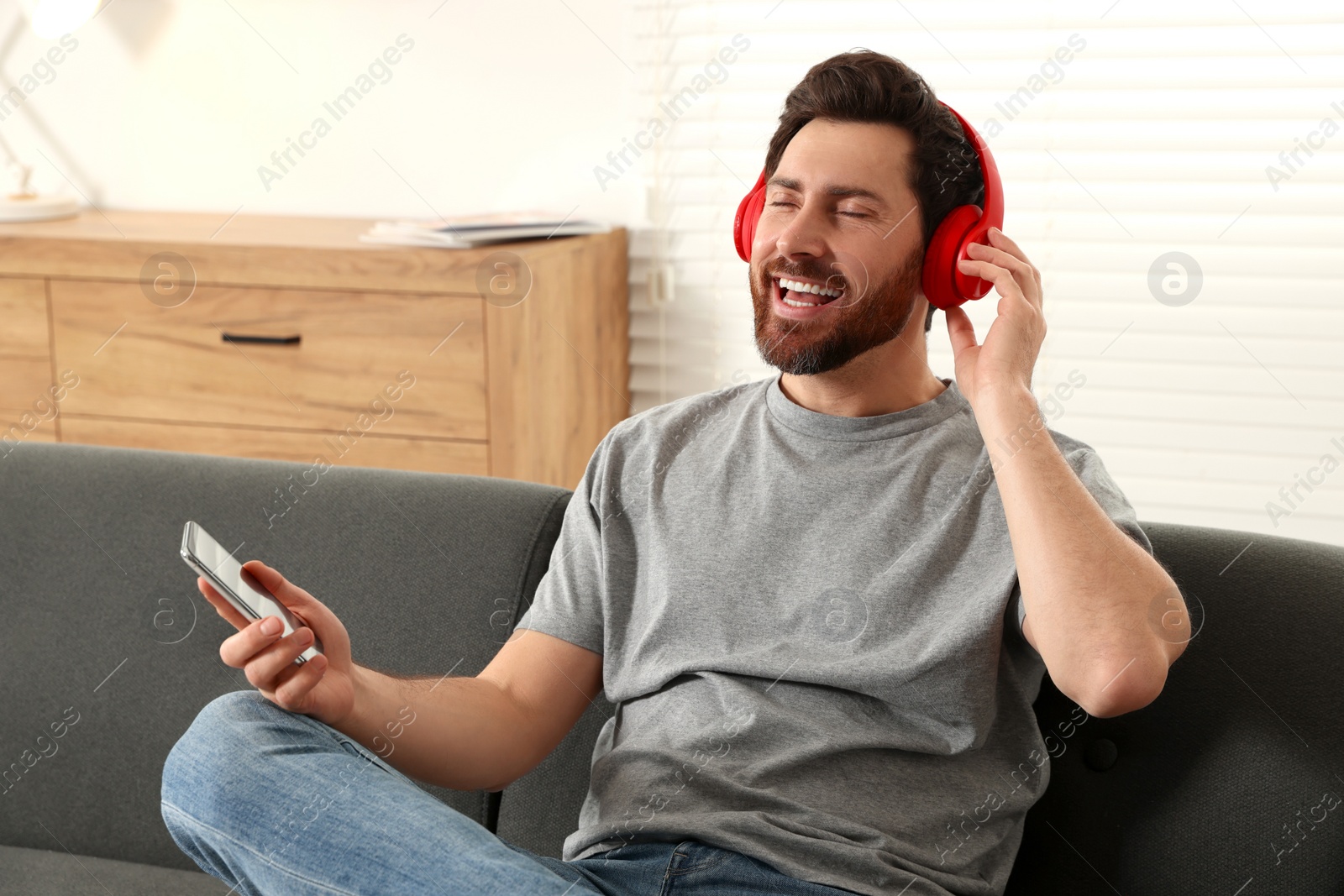 Photo of Happy man listening music with headphones on sofa indoors