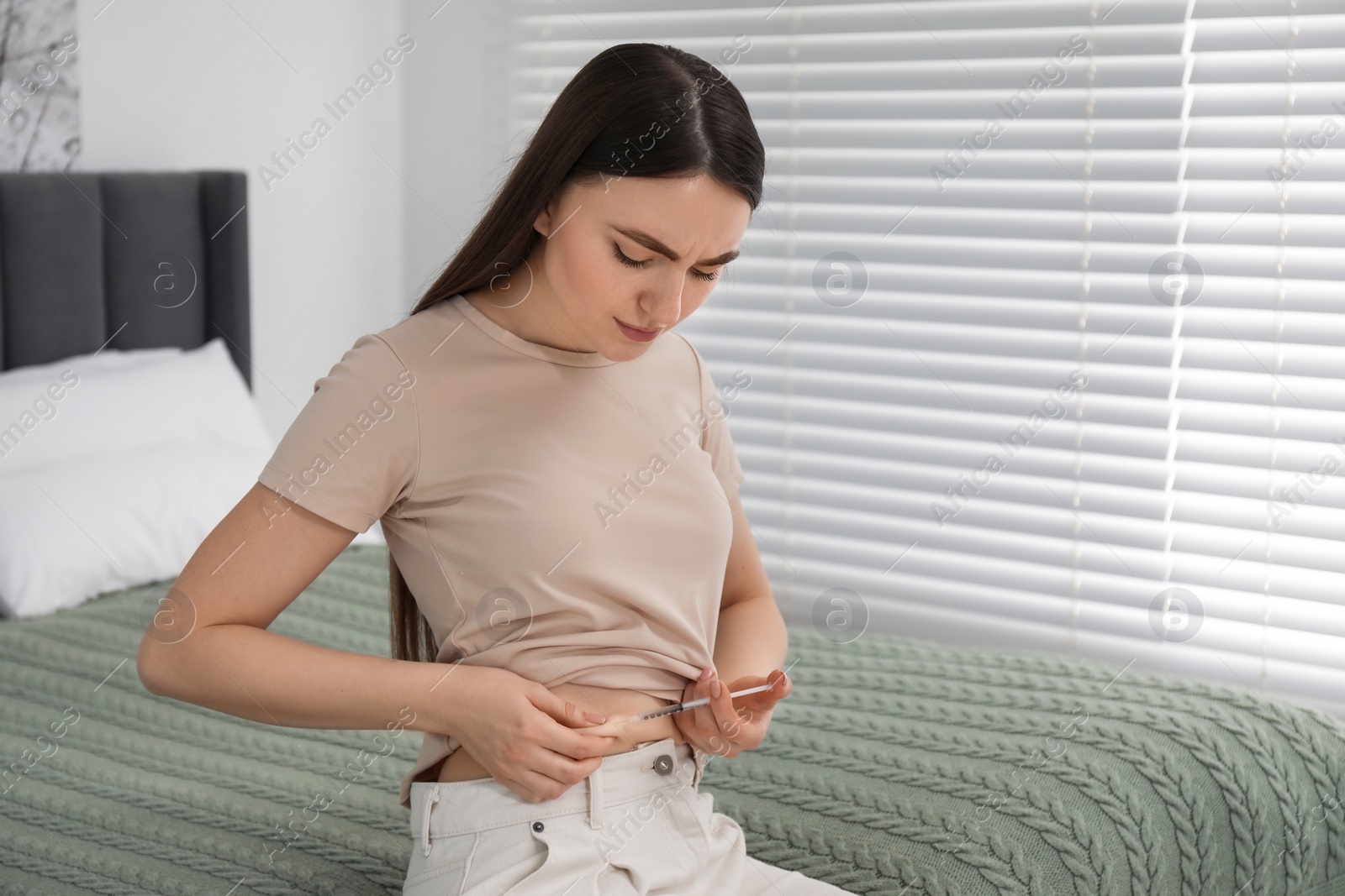 Photo of Diabetes. Woman making insulin injection into her belly on bed in room