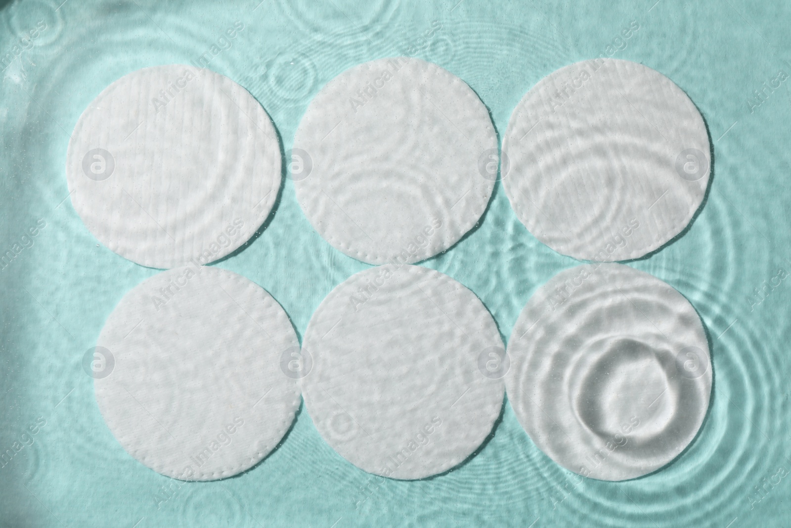 Photo of White cotton pads in water on turquoise background, flat lay
