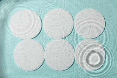 Photo of White cotton pads in water on turquoise background, flat lay