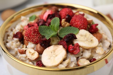 Photo of Delicious oatmeal with freeze dried berries, banana, nuts and mint in bowl, closeup