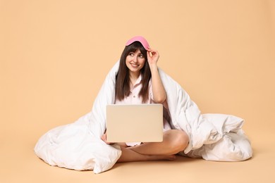 Photo of Happy woman with pyjama and blanket holding laptop on beige background