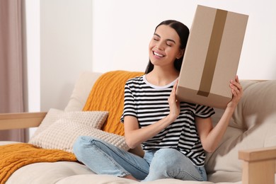 Photo of Happy young woman with parcel on sofa at home. Internet shopping