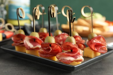 Tasty canapes with olives, prosciutto and cheese on grey table, closeup