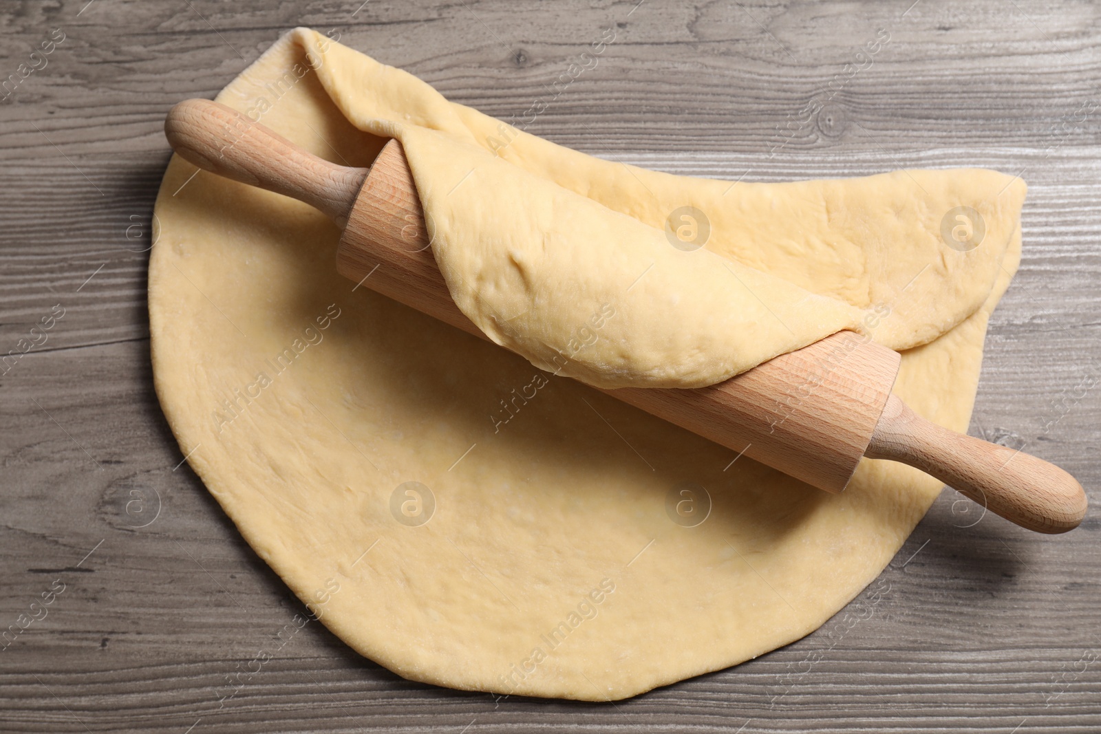 Photo of Raw dough and rolling pin on wooden table, top view