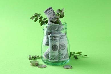Photo of Financial savings. Dollar banknotes in glass jar, twigs and coins on green background