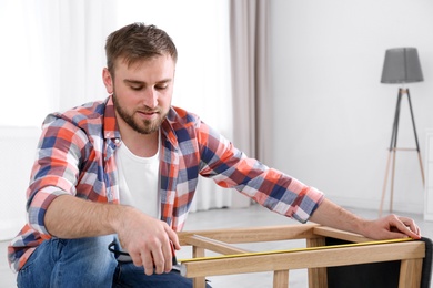 Photo of Young working man using measure tape at home