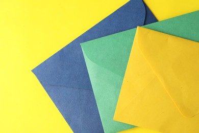 Colorful paper envelopes on yellow background, top view