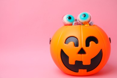 Photo of Halloween trick or treat bucket with different sweets on pink background, space for text