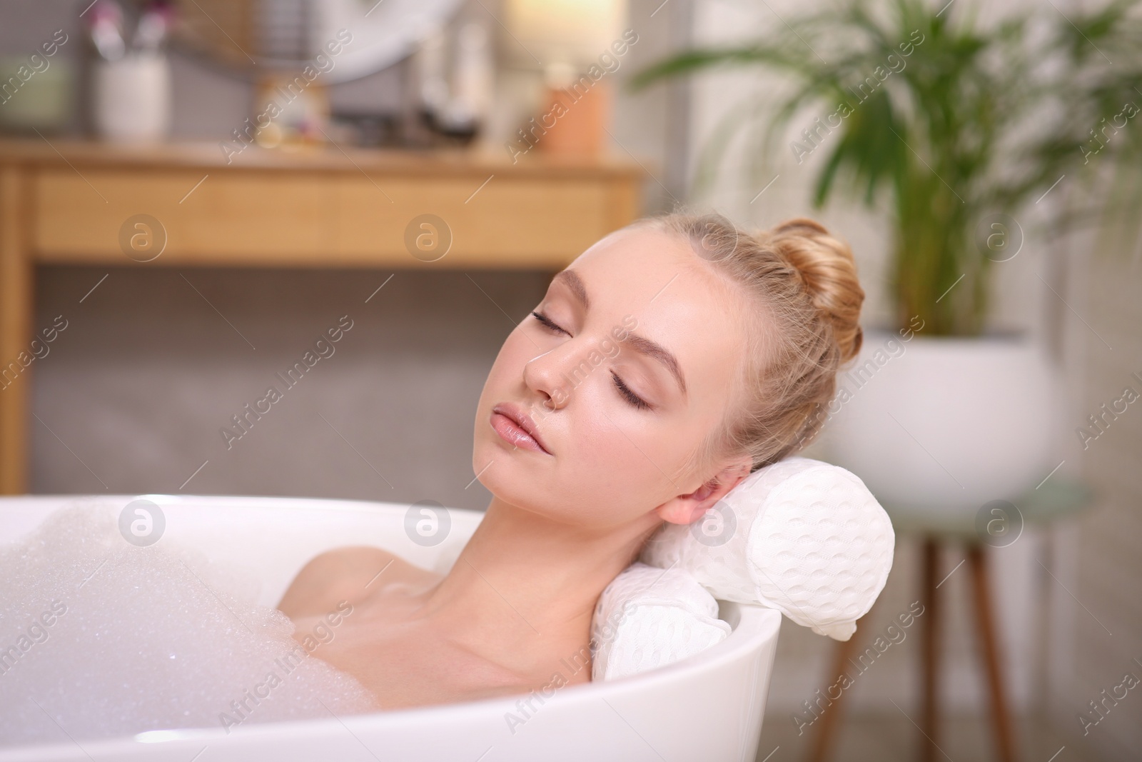 Photo of Young woman using pillow while enjoying bubble bath indoors