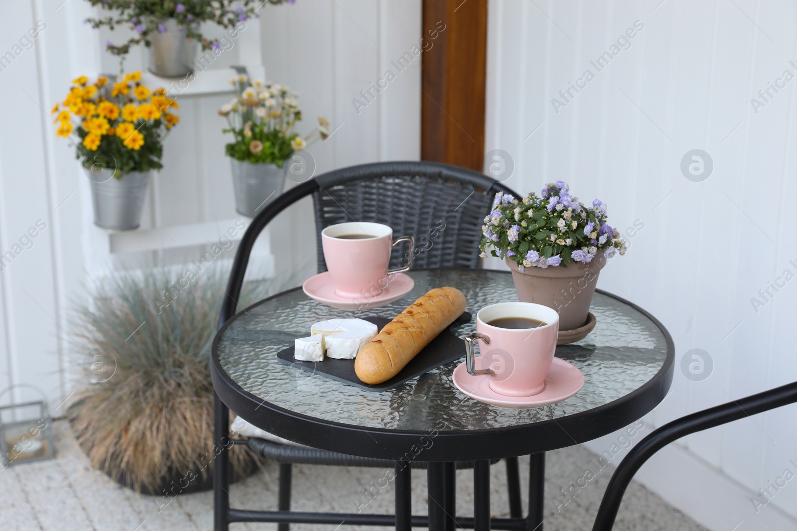 Photo of Cups of coffee, potted plant, bread and cheese on glass table. Relaxing place at outdoor terrace