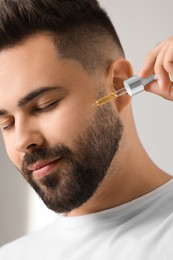 Handsome man applying cosmetic serum onto his face on blurred background, closeup