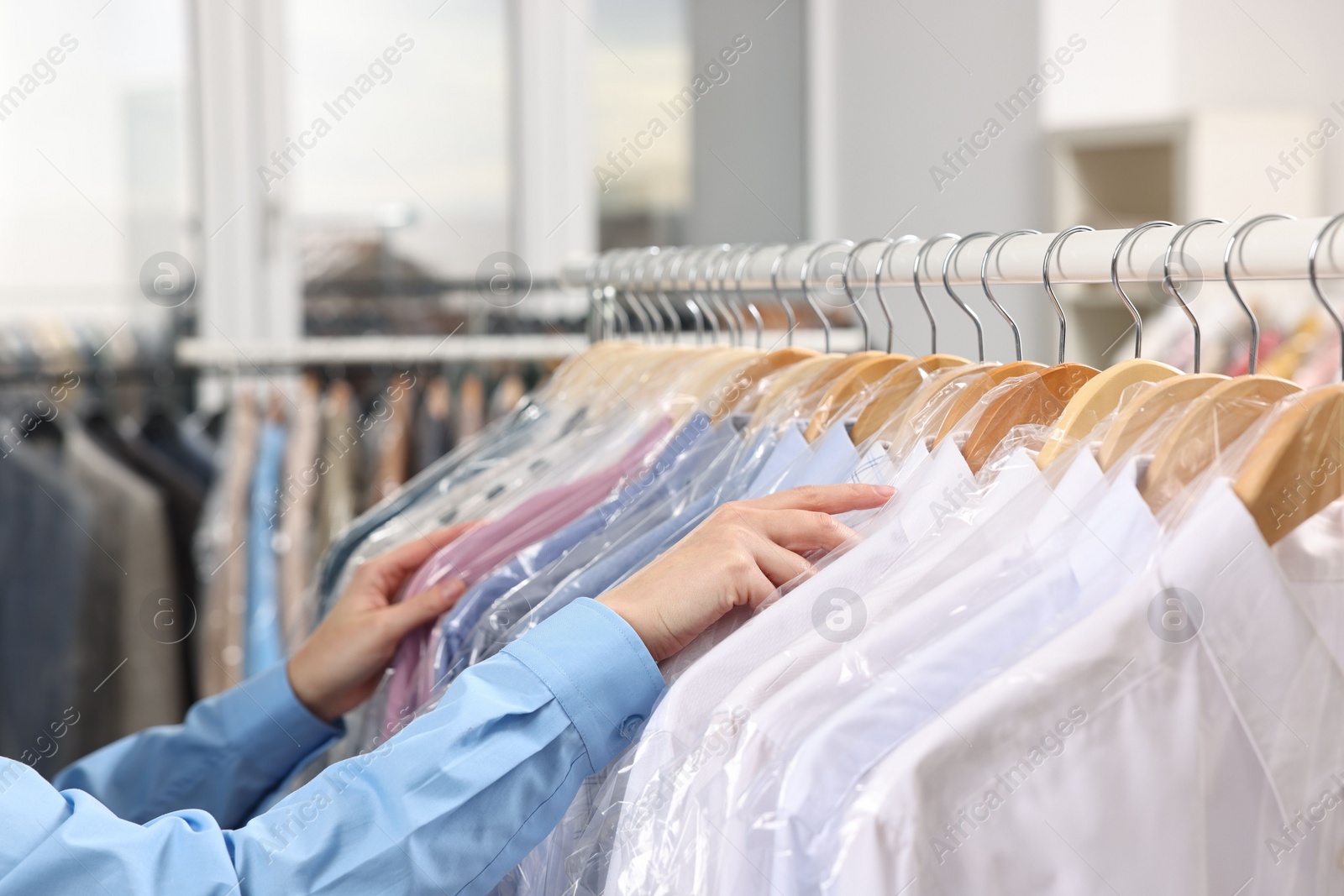 Photo of Dry-cleaning service. Woman taking shirt in plastic bag from rack indoors, closeup