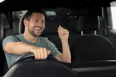 Photo of Listening to radio. Handsome man enjoying music in car, view through windshield