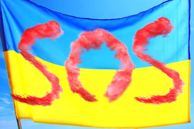 Word SOS made of red smoke and national flag of Ukraine outdoors