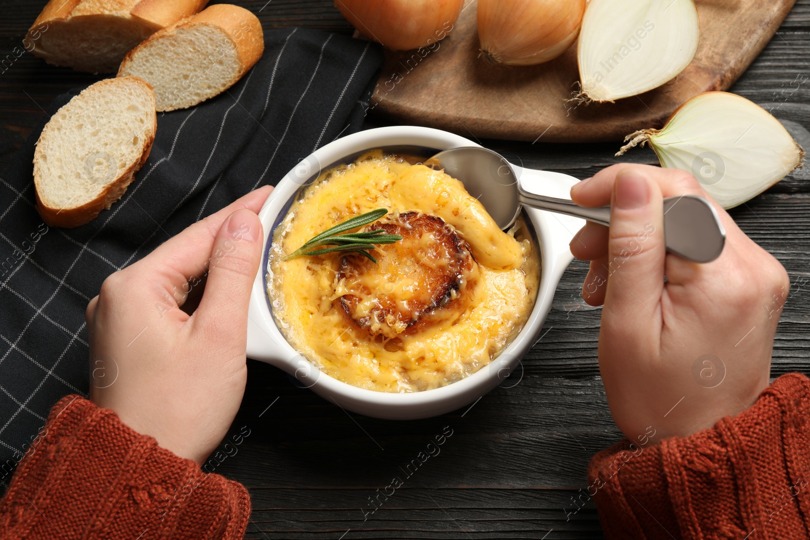 Photo of Woman eating tasty homemade french onion soup at black wooden table, top view