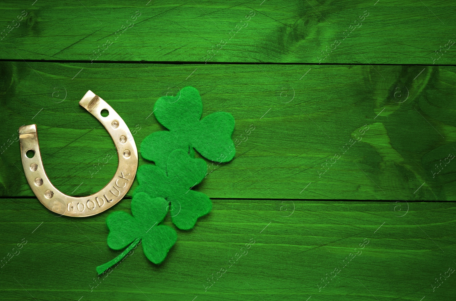 Image of Decorative clover leaves and horseshoe on green wooden background, flat lay with space for text. St. Patrick's Day celebration