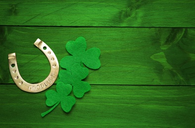 Image of Decorative clover leaves and horseshoe on green wooden background, flat lay with space for text. St. Patrick's Day celebration