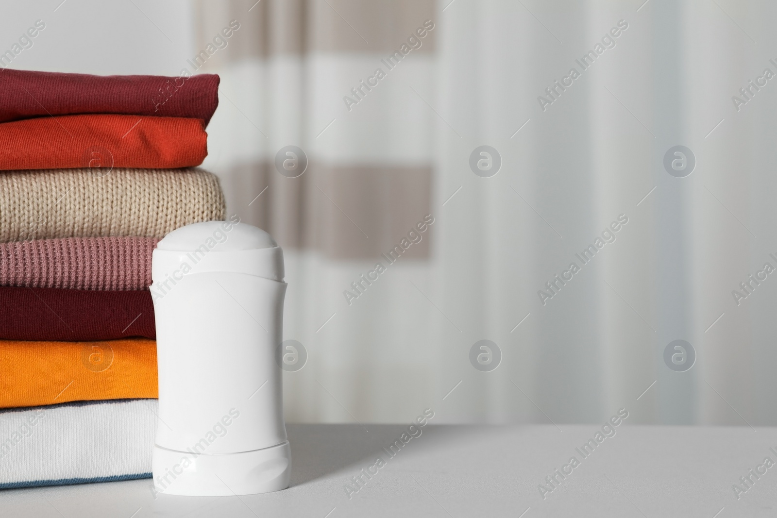 Photo of Deodorant near stack of clean clothes on white table. Space for text