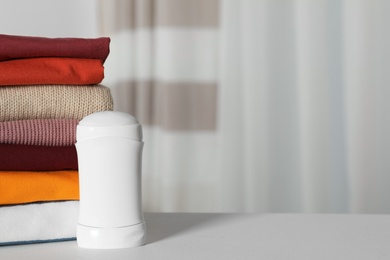 Photo of Deodorant near stack of clean clothes on white table. Space for text