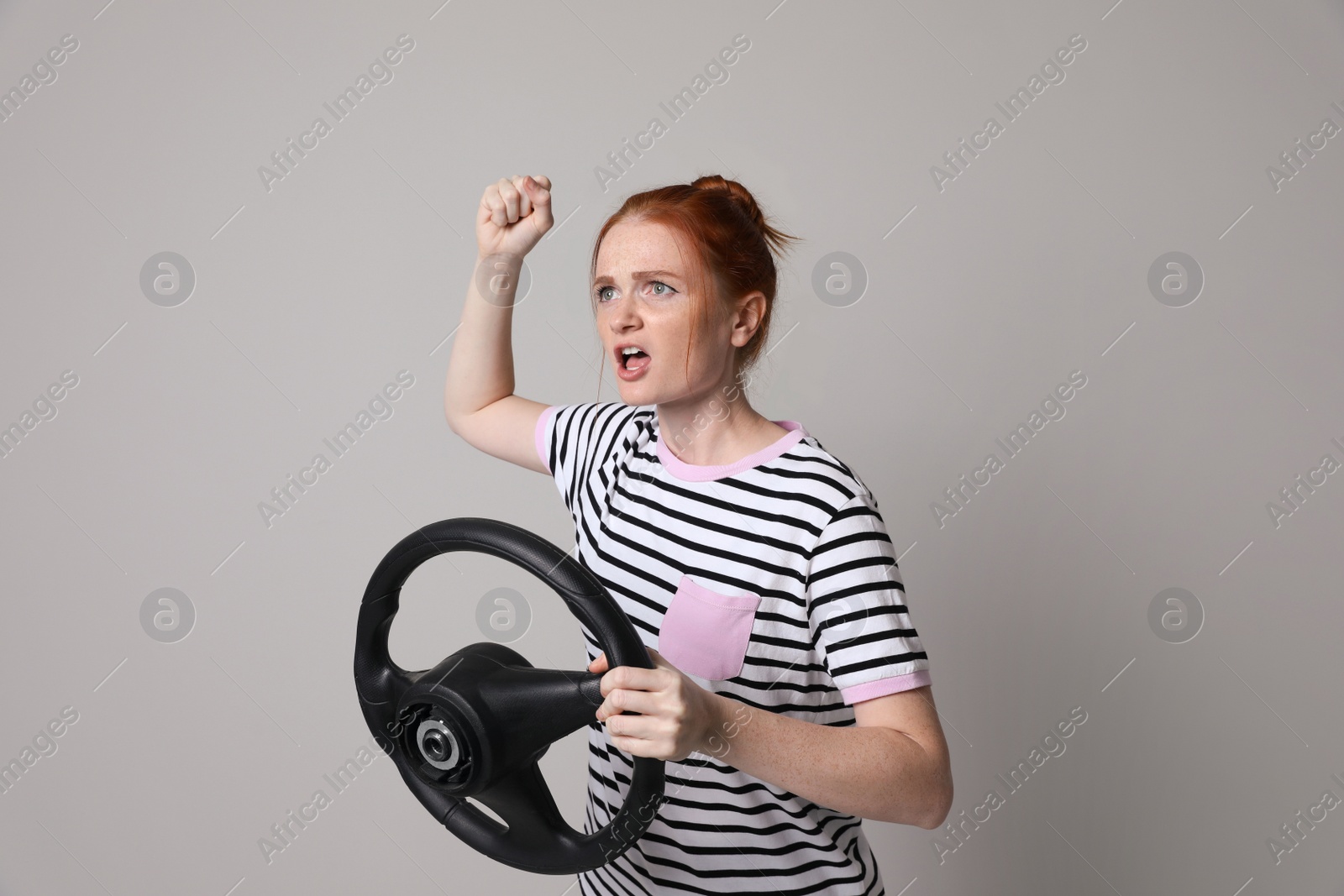 Photo of Emotional young woman with steering wheel on grey background