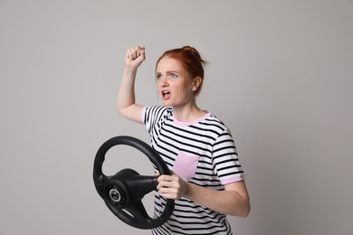 Photo of Emotional young woman with steering wheel on grey background