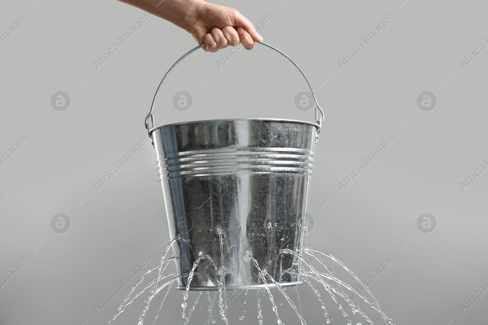 Photo of Woman holding leaky bucket with water on light grey background, closeup