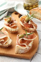 Photo of Tasty sandwiches with cured ham, rosemary and olives on tiled table, closeup