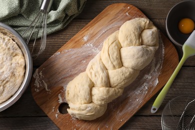 Photo of Homemade braided bread and ingredients on wooden table, flat lay. Cooking traditional Shabbat challah