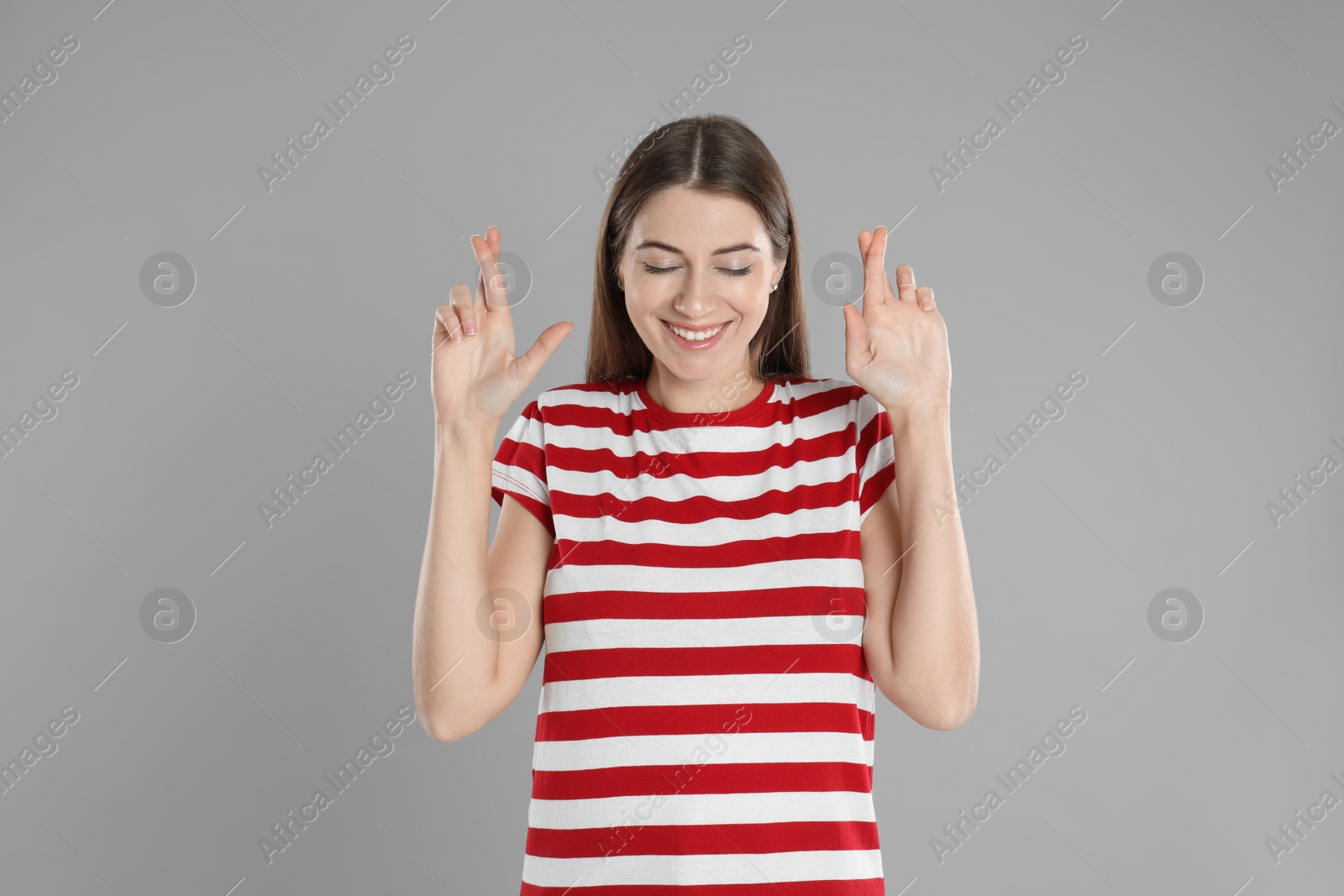 Photo of Woman with crossed fingers on grey background. Superstition concept