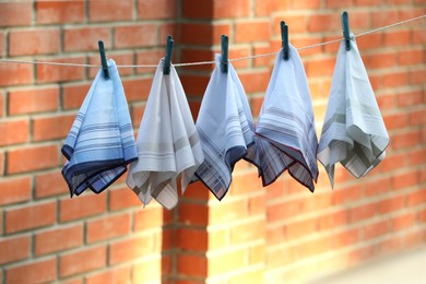 Photo of Different handkerchiefs hanging on rope near red brick wall outdoors
