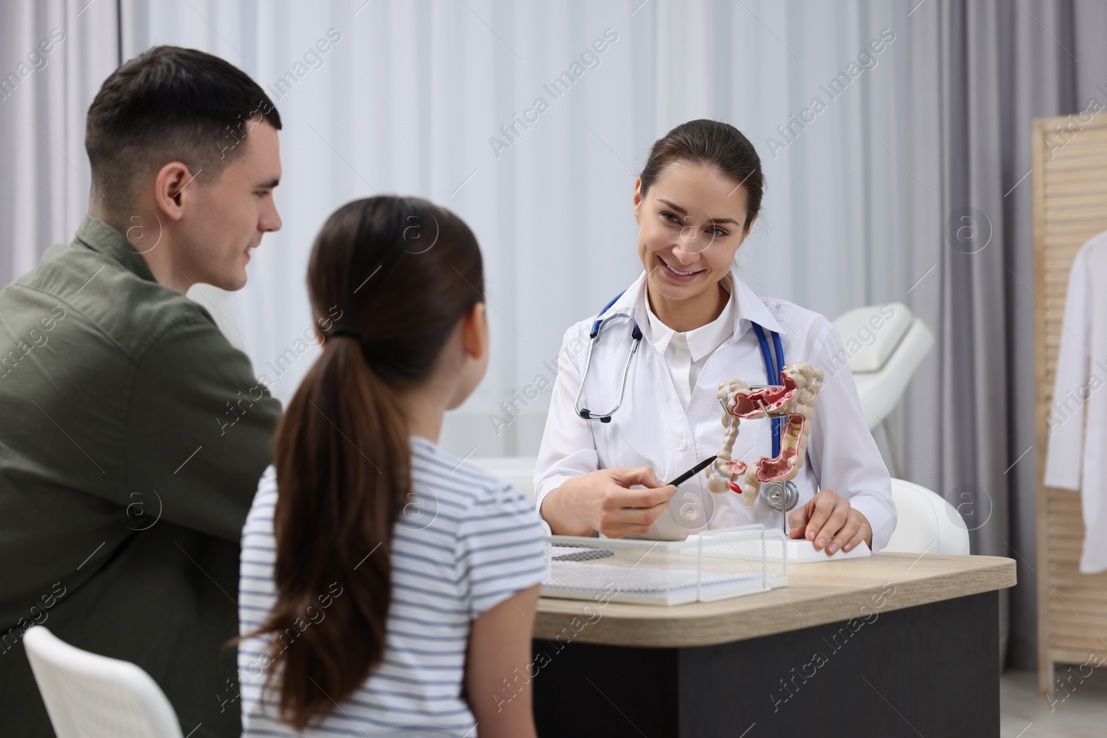 Photo of Gastroenterologist model of intestine consulting man and his daughter in clinic