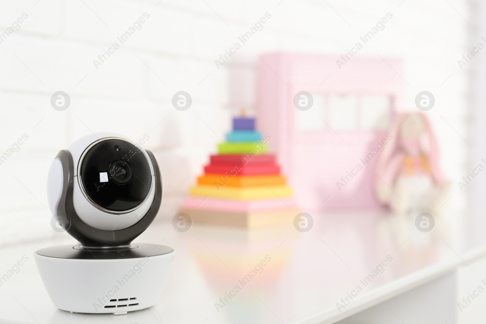 Photo of Baby camera on table near white brick wall, space for text. Video nanny