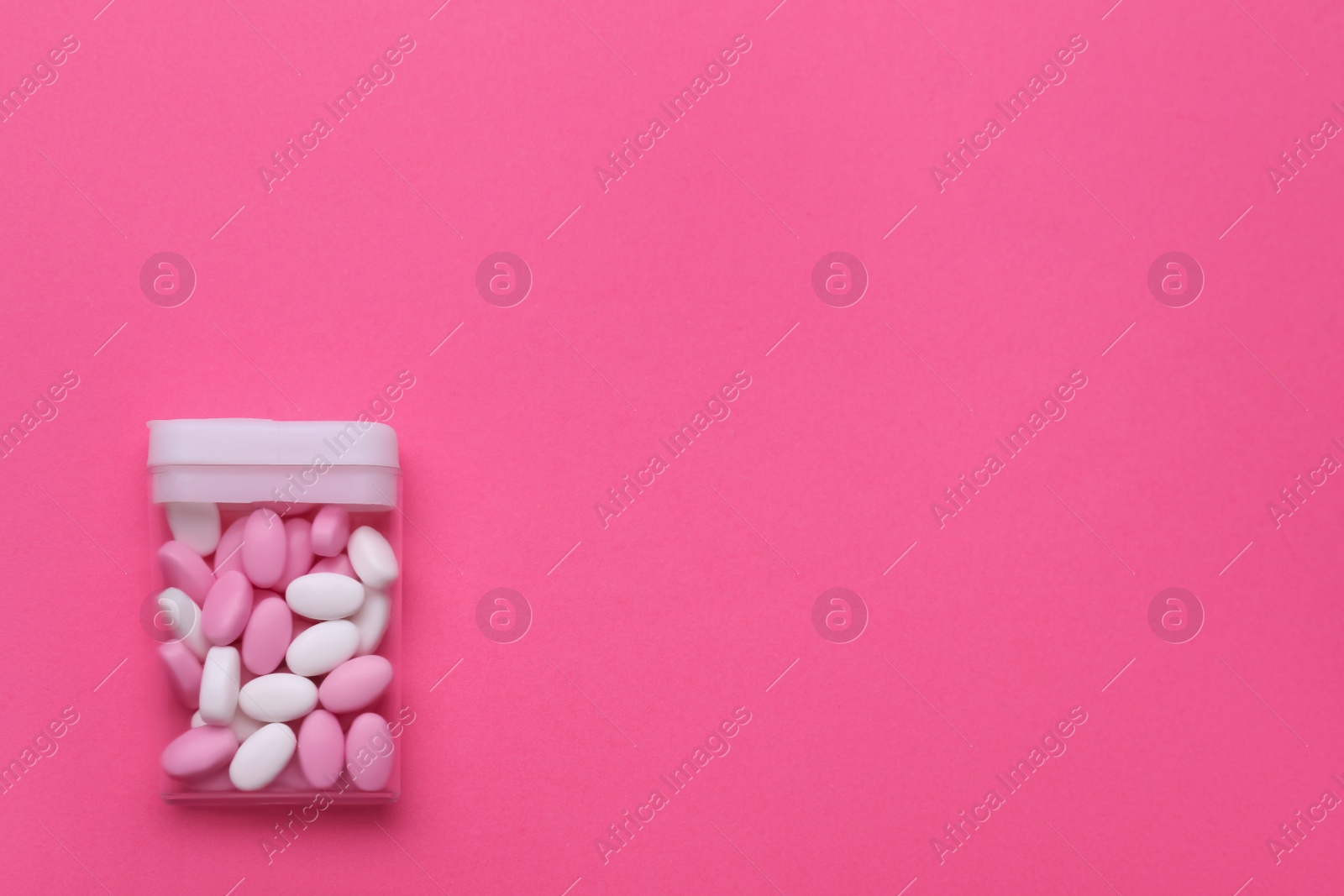 Photo of Many dragee candies in container on pink background, top view. Space for text
