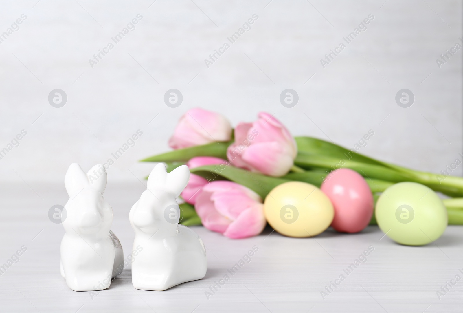 Photo of Cute ceramic bunnies, Easter eggs and spring tulips on table against light background, space for text