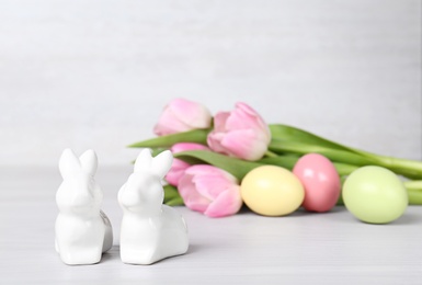 Photo of Cute ceramic bunnies, Easter eggs and spring tulips on table against light background, space for text