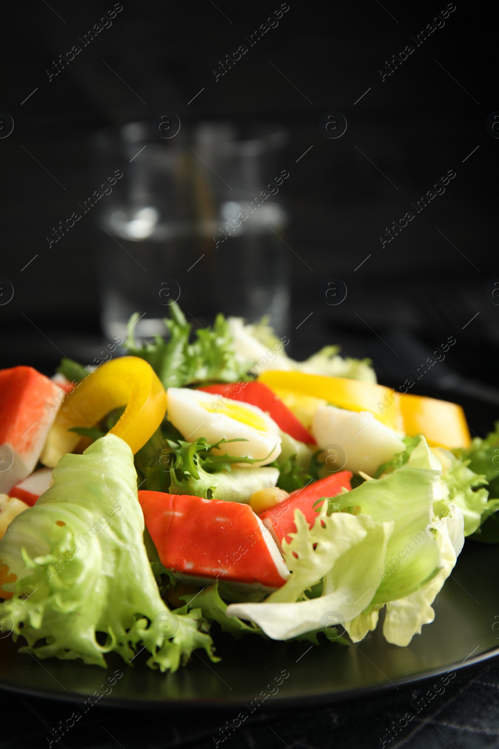 Photo of Salad with crab sticks and lettuce on black plate, closeup