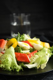 Salad with crab sticks and lettuce on black plate, closeup