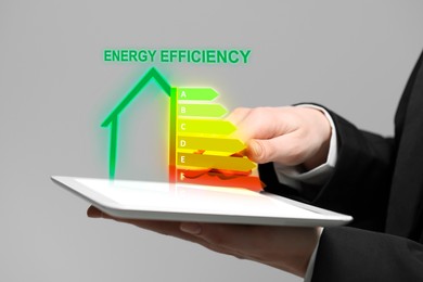 Image of Energy efficiency rating coming out of tablet. Man using device on light background, closeup