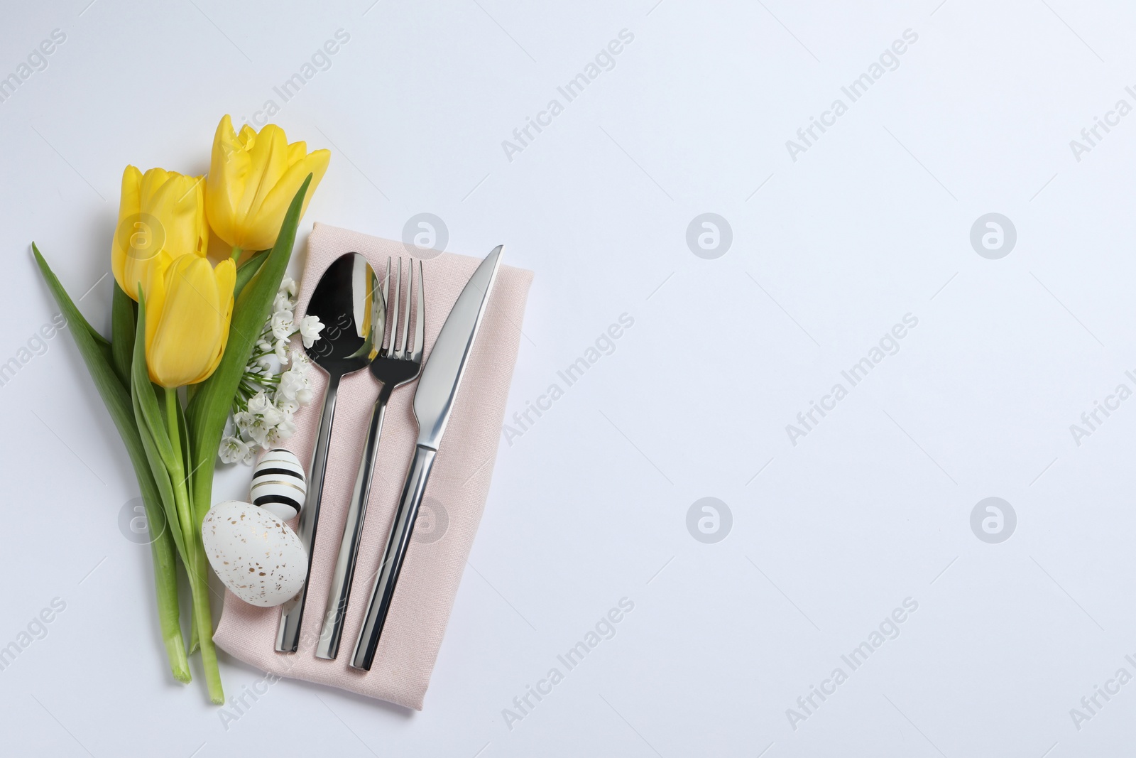 Photo of Cutlery set, Easter eggs and beautiful flowers on white background, flat lay with space for text. Festive table setting