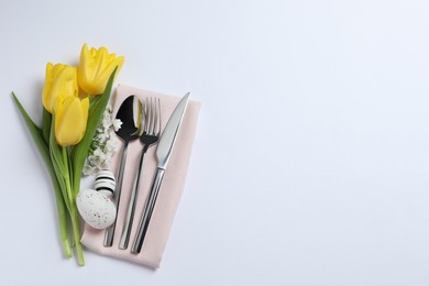 Photo of Cutlery set, Easter eggs and beautiful flowers on white background, flat lay with space for text. Festive table setting