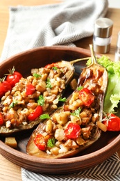 Photo of Bowl with tasty stuffed eggplants on wooden table, closeup