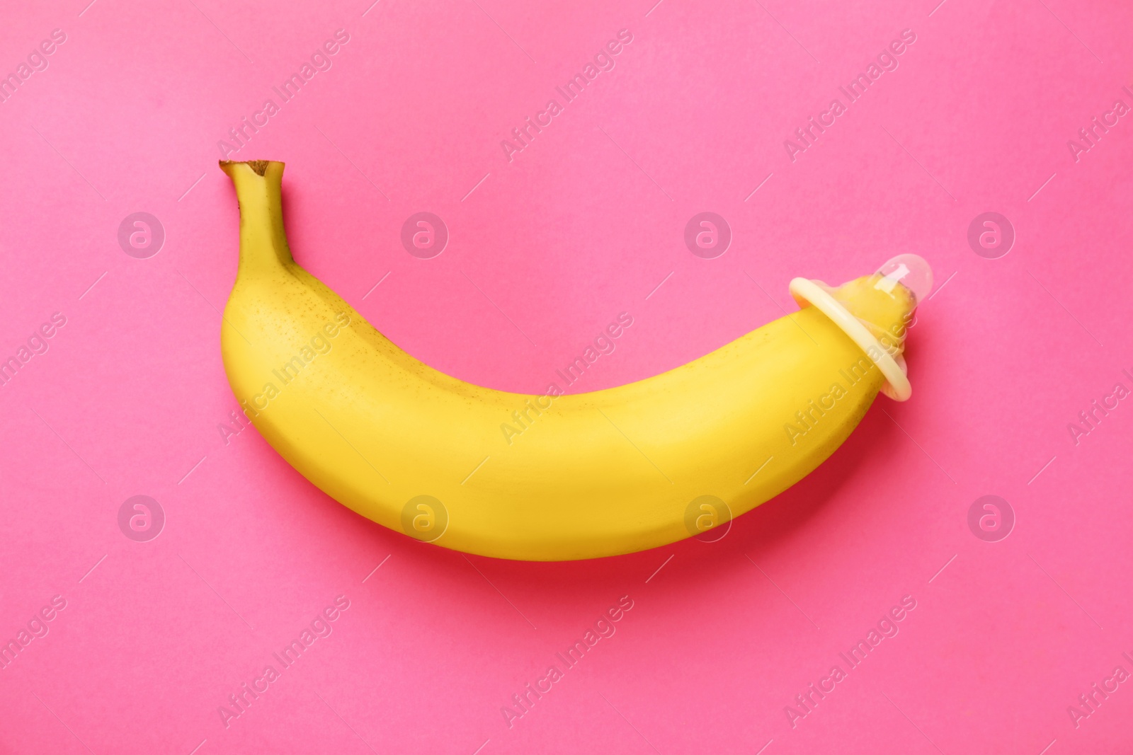 Photo of Banana with condom on pink background, top view. Safe sex concept