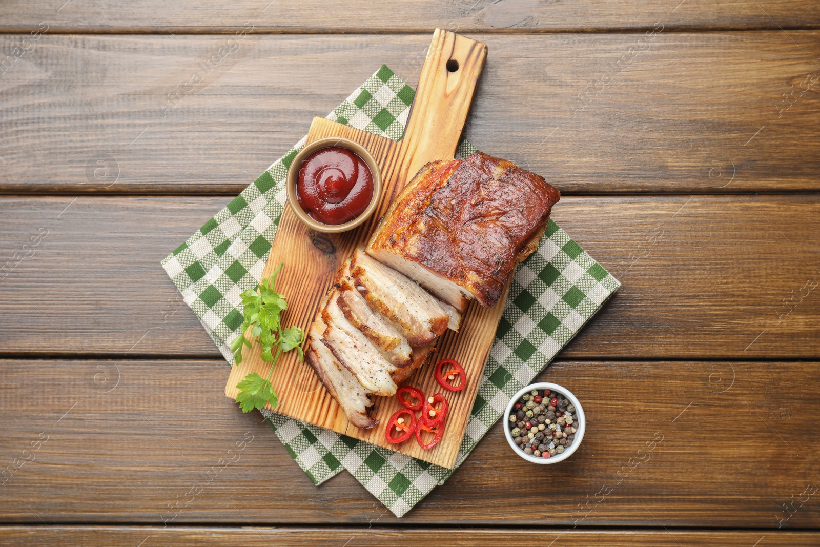 Photo of Pieces of baked pork belly served with sauce, chili pepper and parsley on wooden table, top view