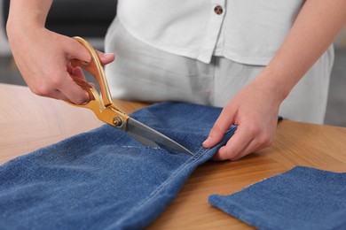 Woman making ripped jeans at wooden table, closeup