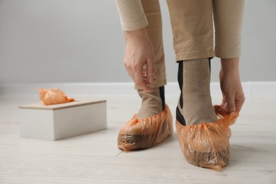 Photo of Woman wearing bright shoe covers onto her boots indoors, closeup